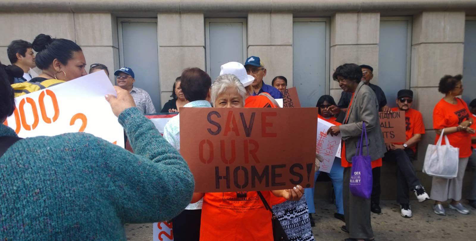 A group of Right to Counsel activists meet. One holds a sign reading Save Our Homes